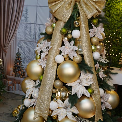 Árvore de Natal dourada com laço gigante de tecido dourado e poinsétias claras.