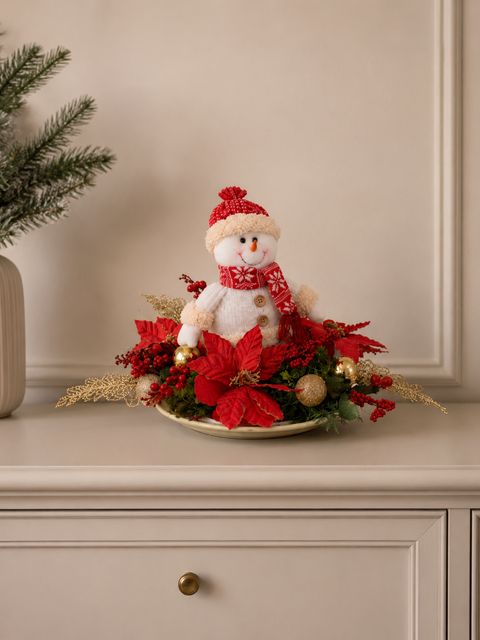 Centro de mesa natalino com boneco de neve, poinsétias vermelhas e dourados.